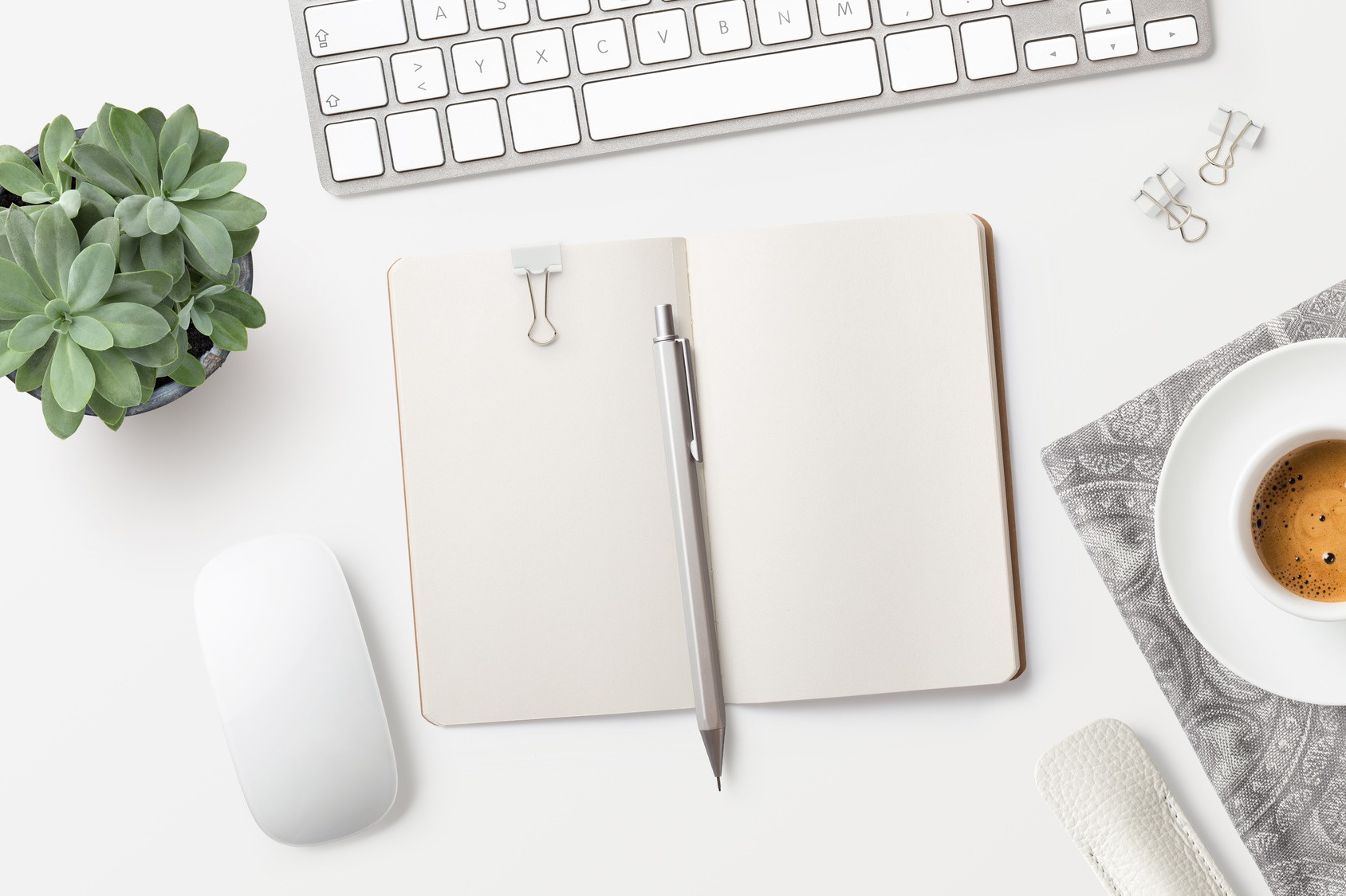 Desktop with blank open notebook, coffee, office supplies and succulents on a white table
